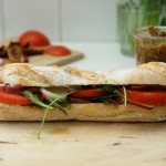 Selbst gebackenes Ficelle mit Oregano-Nuss-Pesto, Tomaten, roten Zwiebeln und Rucola