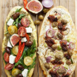 Zwei wunderbare griechische Pizzen mit Rucola, Tomaten, Champignons, grünen Oliven, Kalamata Oliven, Oliven- und Tomatenpaste